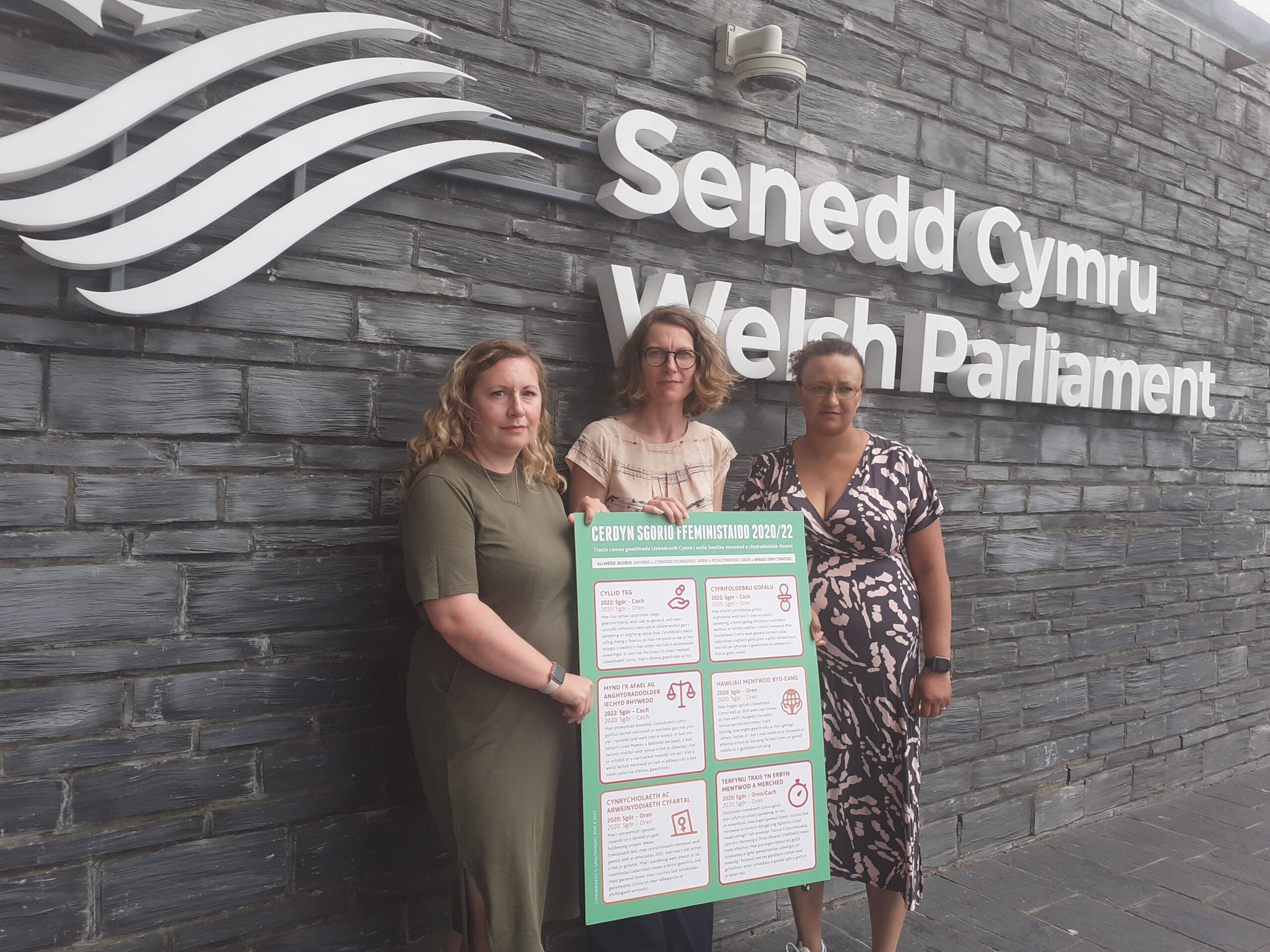 Three women pose with a large version of the feminist scorecard